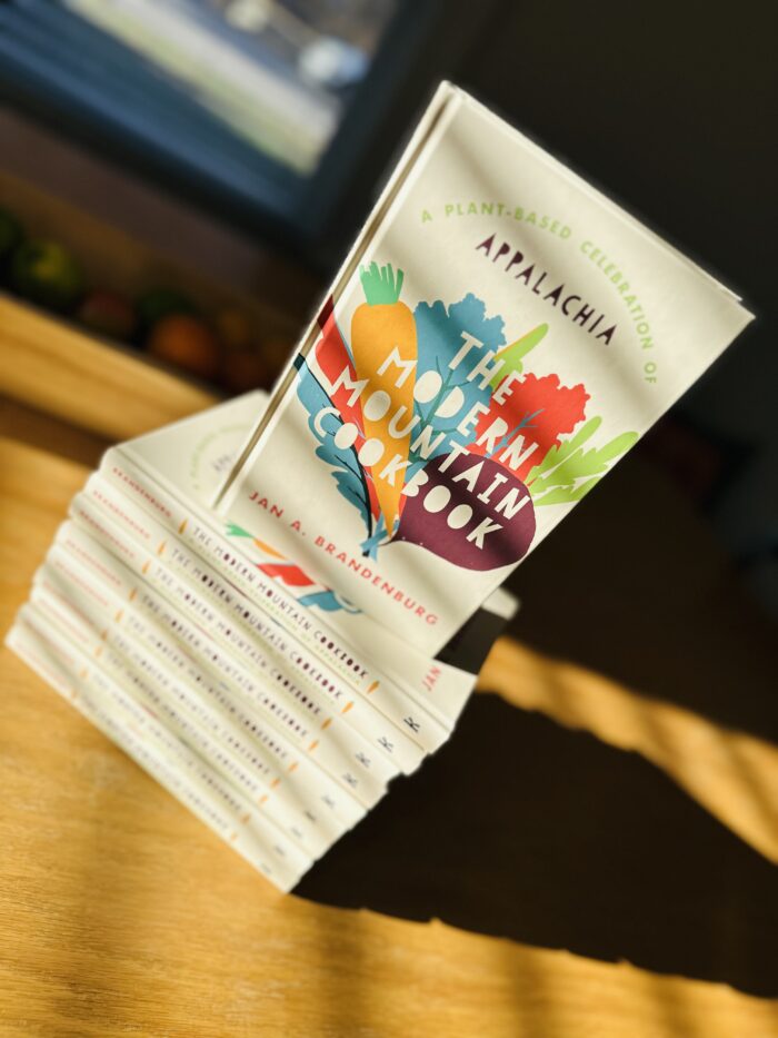 A book on a table with the title, "The Modern Mountain Cookbook: A Plant-Based Celebration of Appalachia" and the author's name "Jan A. Brandenburg".